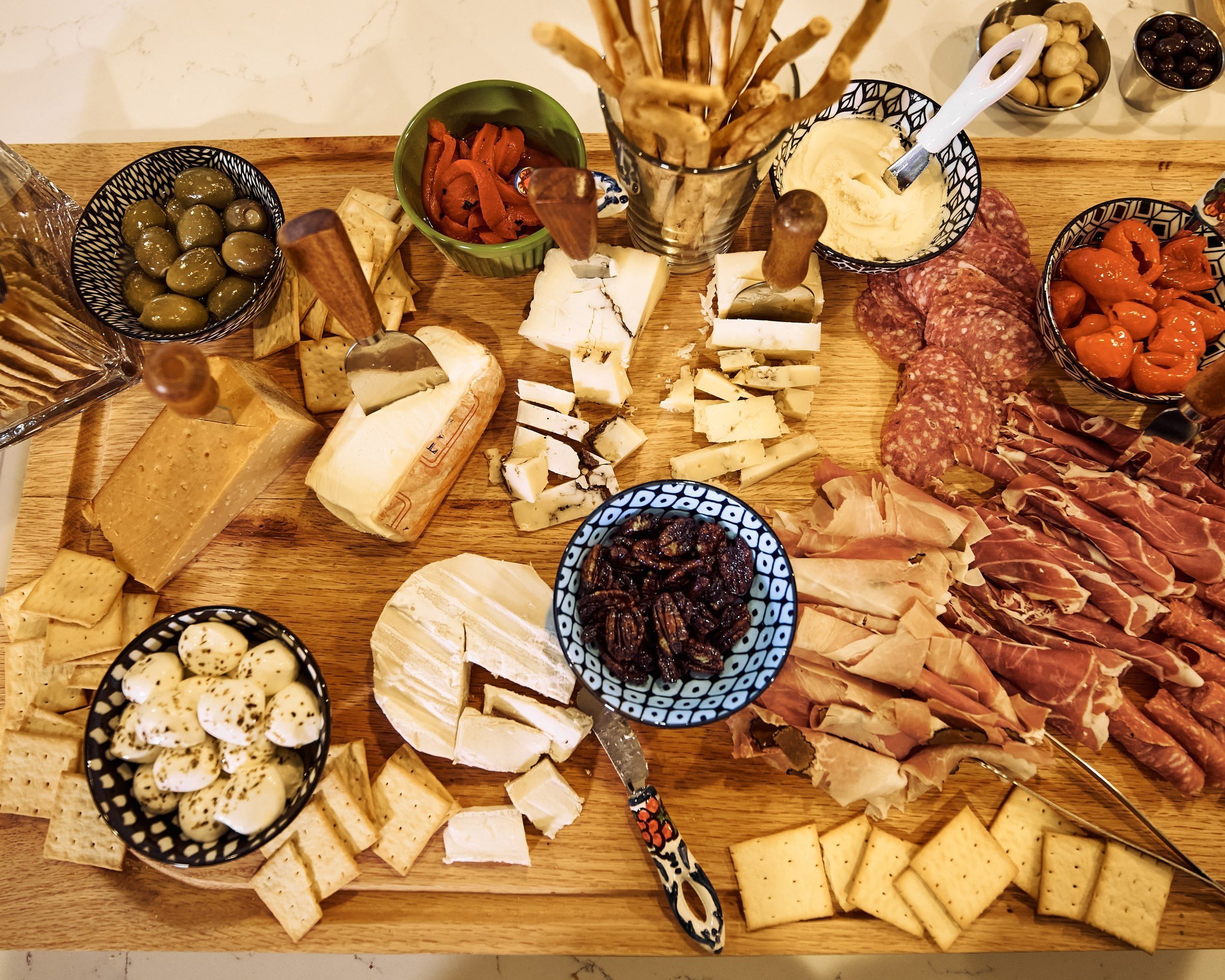 A charcuterie board from above: cheeses, cured meats, olives, peppers and crackers.