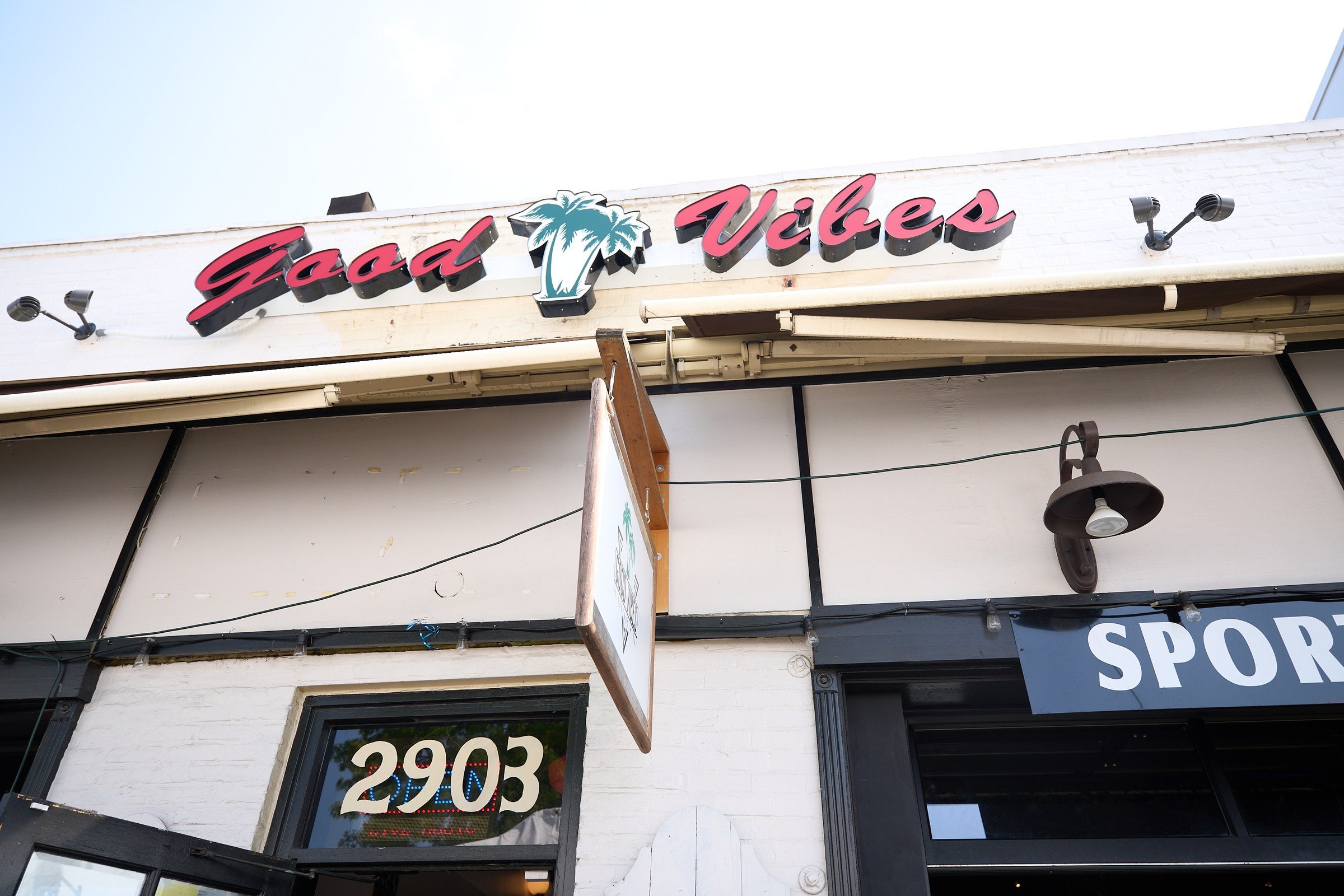 The front of the old Good Vibes: a red script Good Vibes sign with a teal palm tree between the words, above a door numbered 2903.
