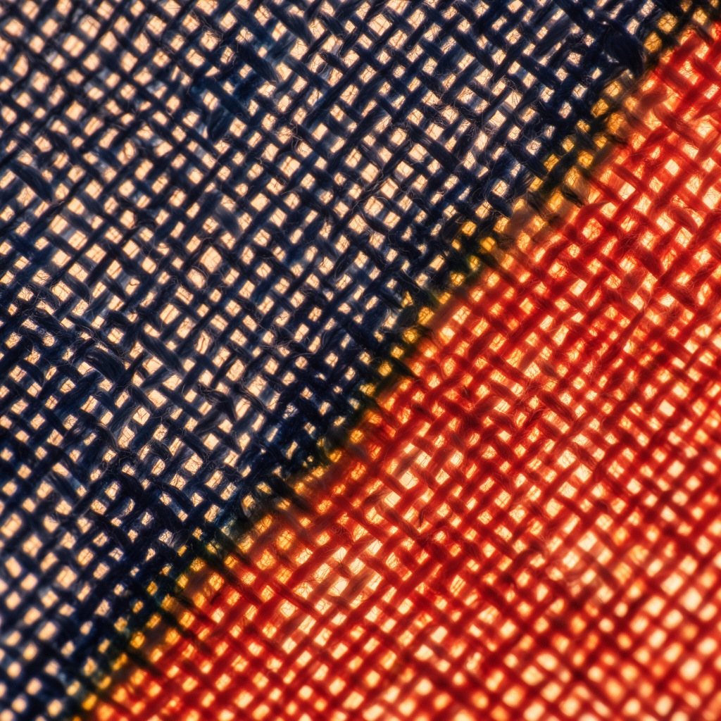Macro of the cotton weave glowing against the light, indigo meeting vermilion.