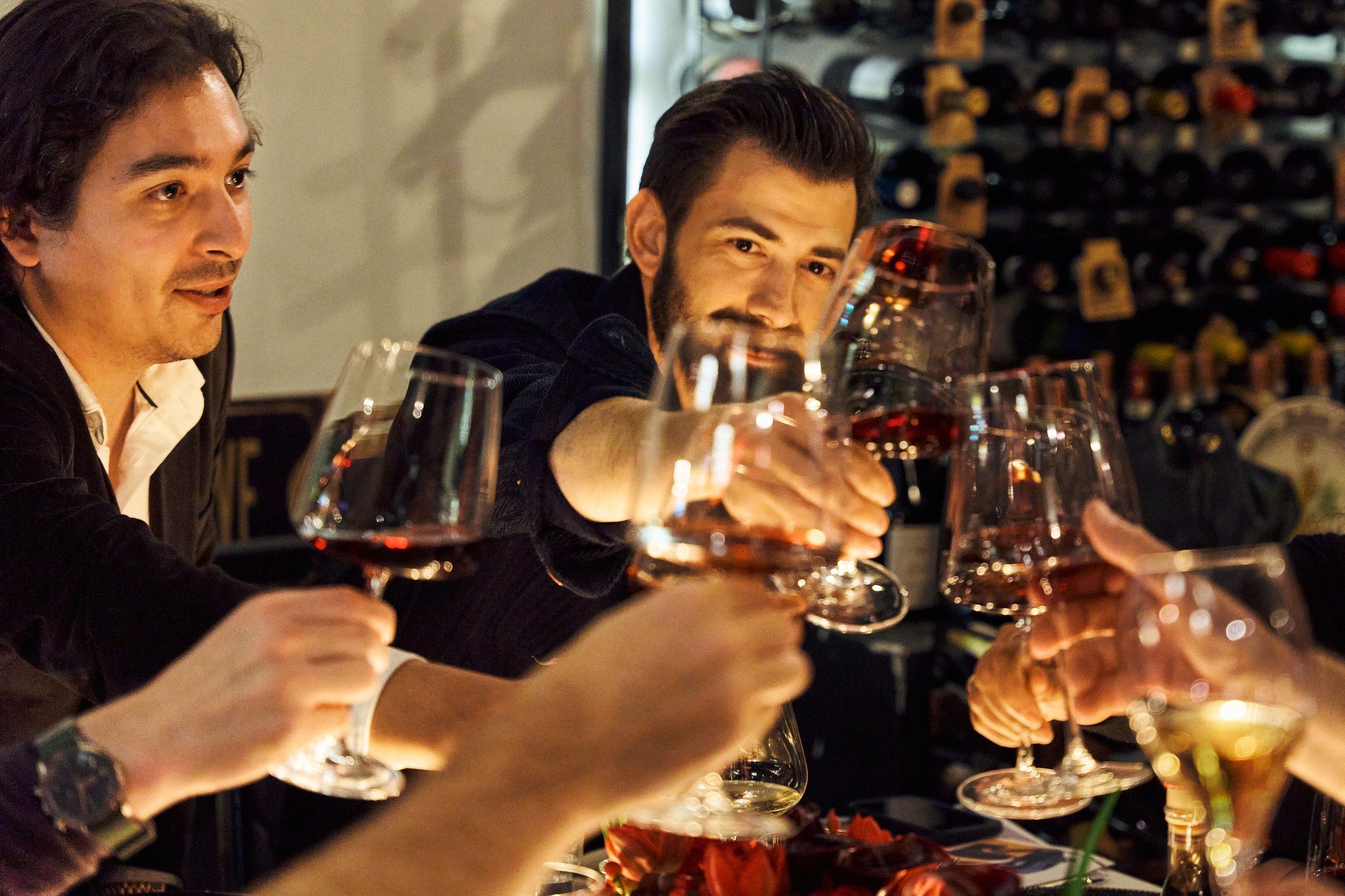 Two guests laughing and raising wine glasses at the table.