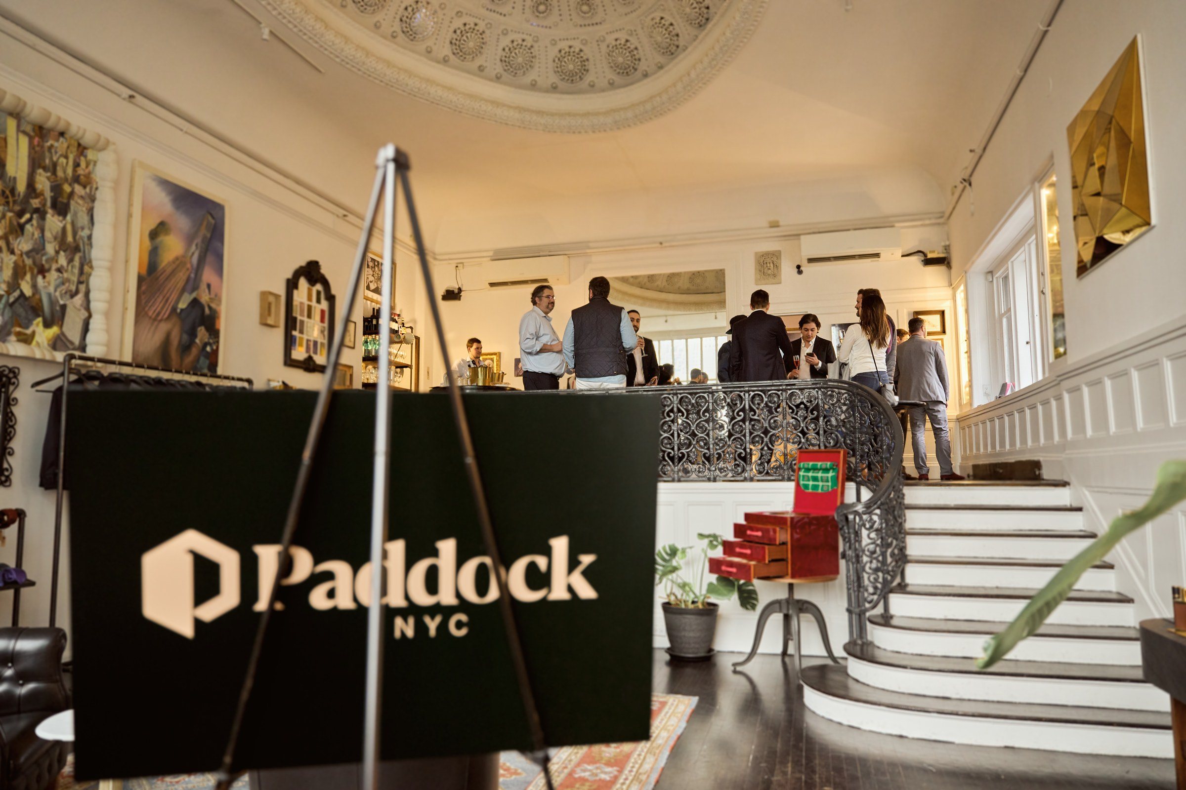 Guests on a sweeping staircase in a townhouse atelier, a Paddock NYC sign on an easel.