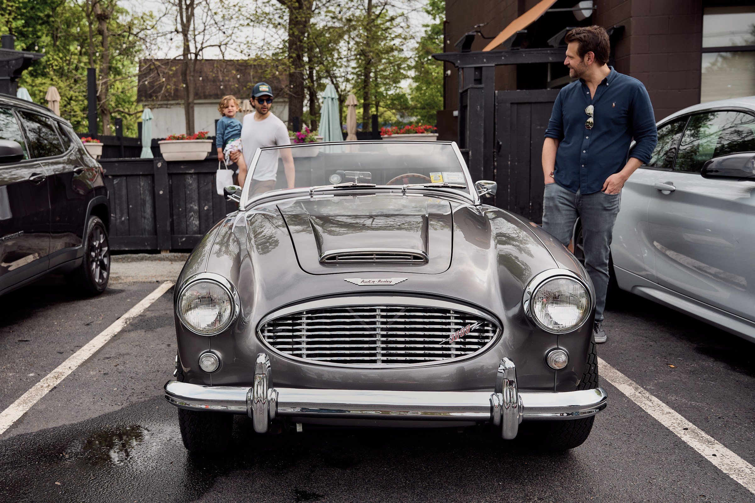 A silver Austin-Healey roadster among the rally cars, a driver standing by.